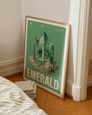 Vintage-inspired May birthstone poster featuring a watercolour emerald illustration in green background. White bedroom with large framed poster with May crystal illustration.