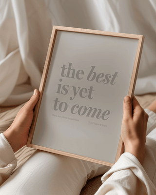 The Best Is Yet To Come print in natural wooden frame. Woman holds the print while she lays down