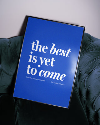 The Best Is Yet To Come blue print in black frame sitting on blue velvet sofa
