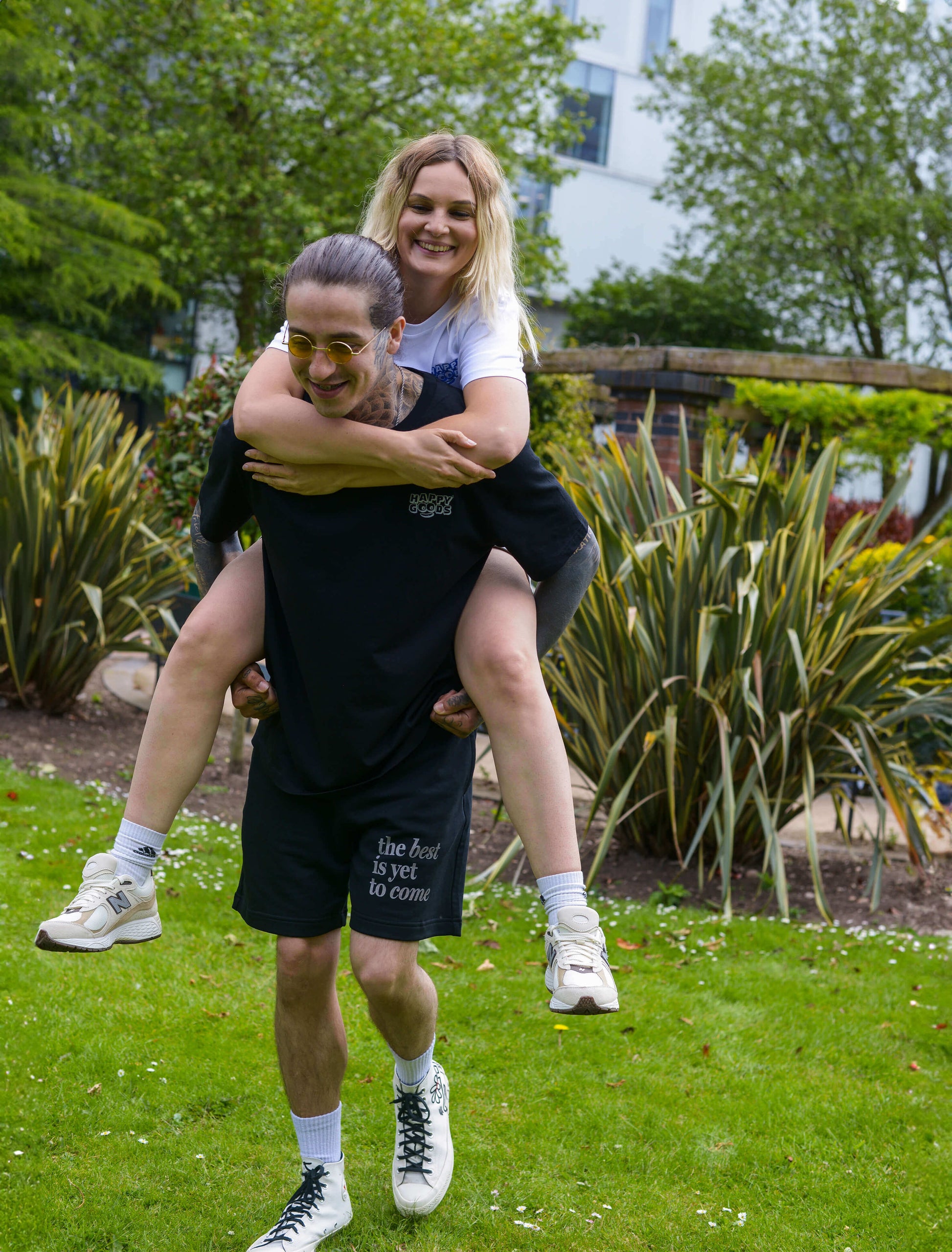 The best is yet to come shorts. positive messaging mental health shorts. Male and female model having piggy back rides in the park