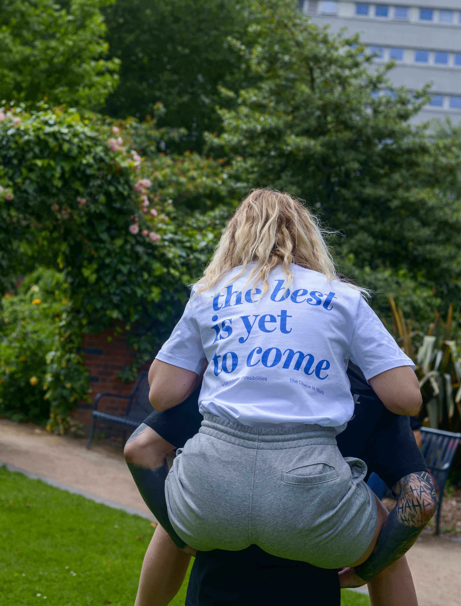 The best is yet to come t-shirt. positive messaging mental health tee. woman having fun getting piggy back ride. city scene 