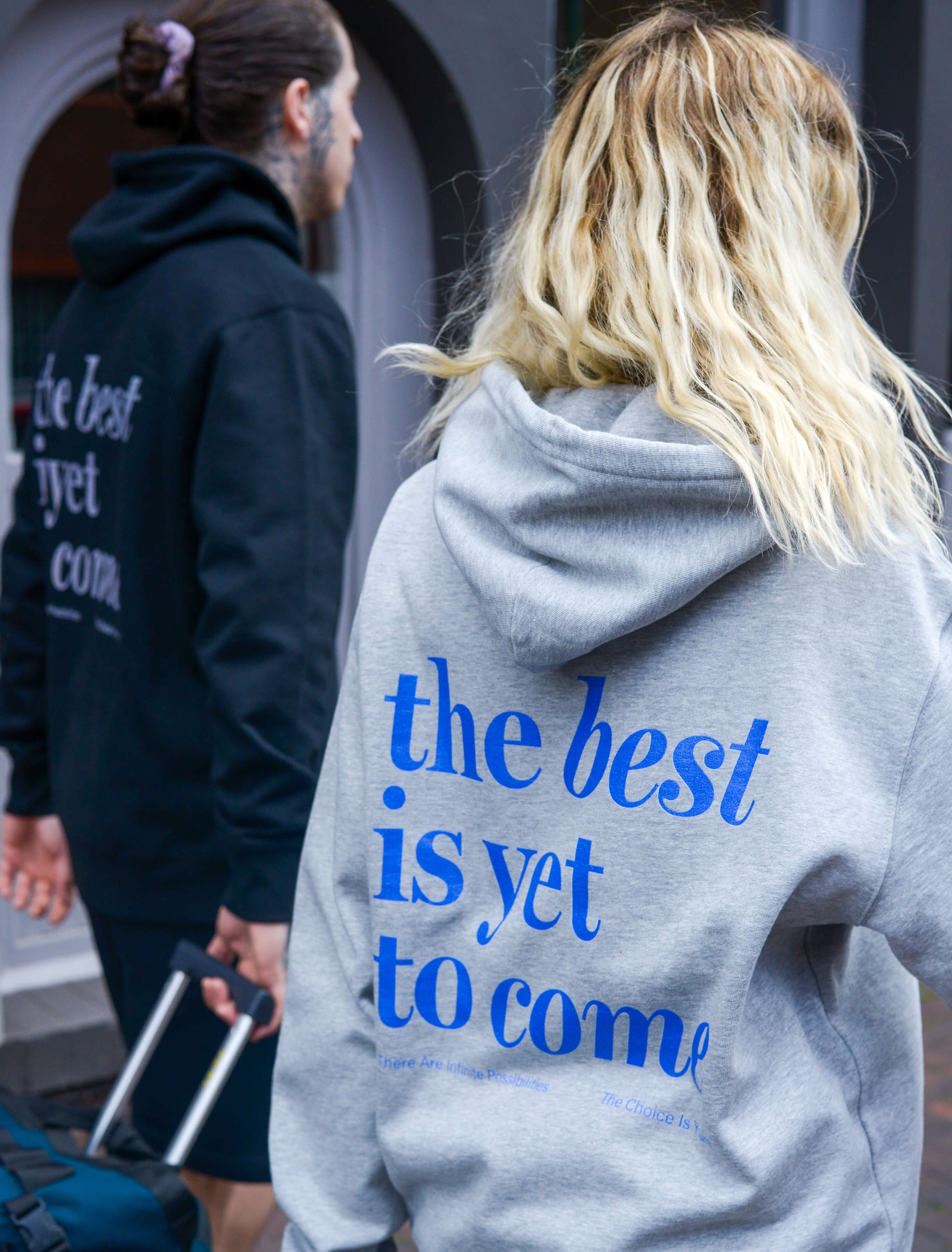 The best is yet to come hoodie. positive messaging mental health hoodie. airport outfit. airport style. Pair of models wearing matching hoodies on route to their holiday