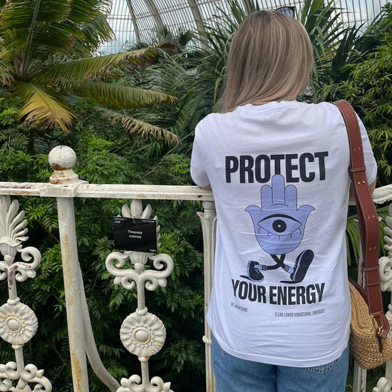 Woman wearing protect your energy t-shirt in nature. Purple hamsa hand design, high vibe