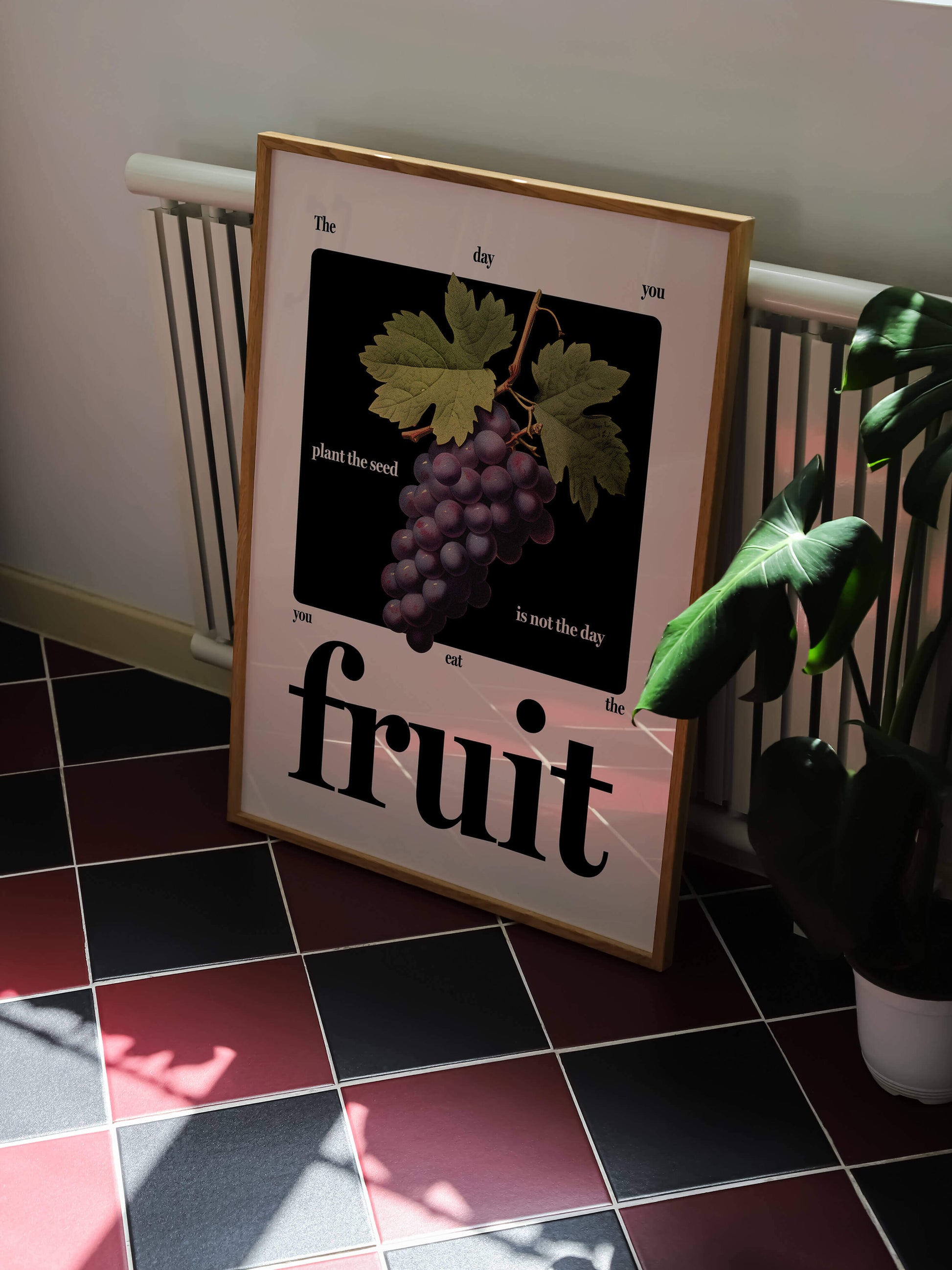 Motivational fruit art print framed rests against radiator next to plant in kitchen on stunning tiled floor.