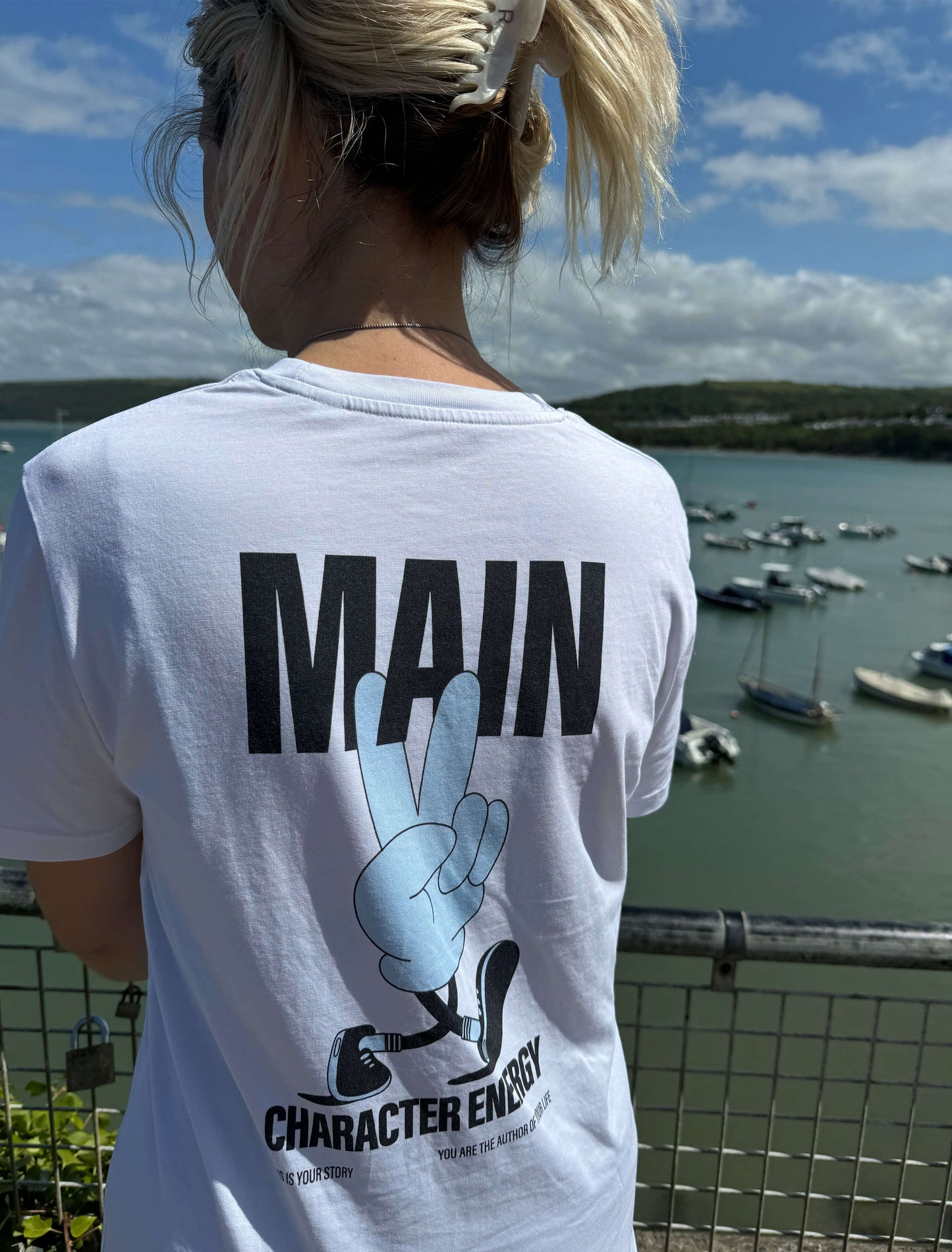 Main character energy tee in blue on holiday, overlooking beach and boats