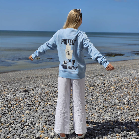 Woman wearing protect your energy sweater on the beach. Wellbeing, mental health jumper