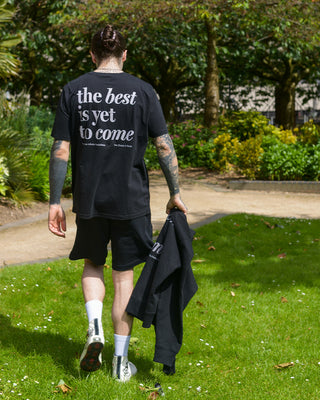 The best is yet to come t-shirt. positive messaging mental health tee. black and grey. Man walks through park wearing essential t-shirt. Holds positive hoodie in his hand