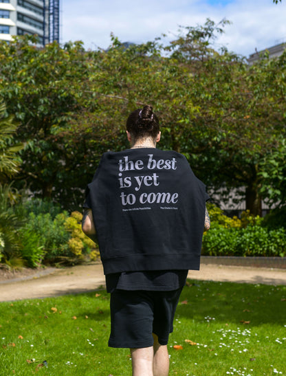 The best is yet to come hoodie in black. Man wearing positive messaging clothing mental health hoodie in black. Man wearing hoodie loosely over shoulders in park