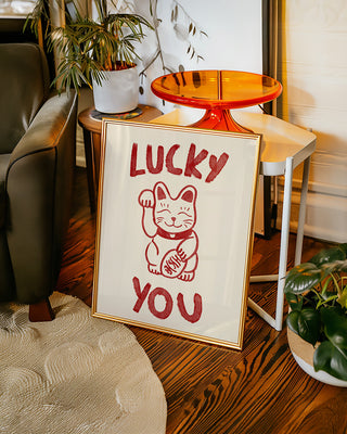 Lucky you unique wall art print in a gold frame in retro living room. The art print is hand drawn and features a drawing of Japanese lucky cat. The poster is in cream and cherry red. Contemporary wall art gift for loved ones, anniversaries or Valentine's day.