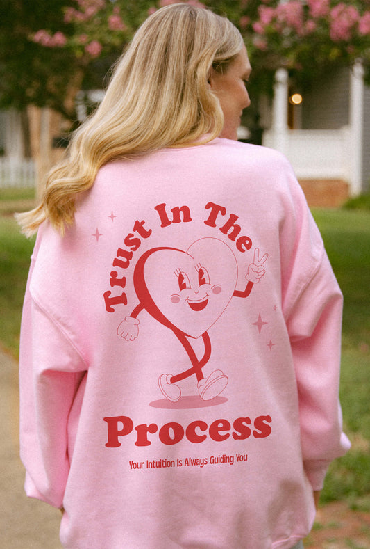 Woman wearing pink sweater with positive messaging that says trust in the process