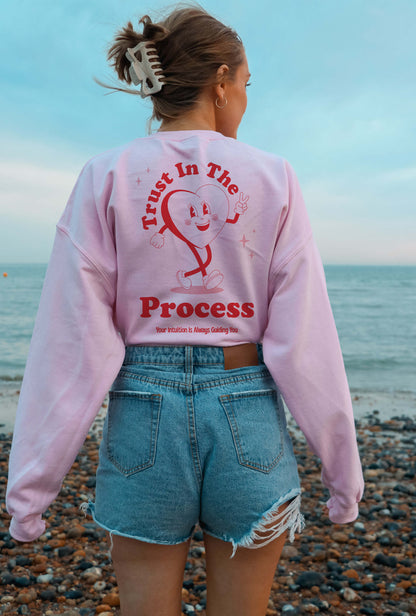 woman is wearing pink positive Trust in the process sweater on the beach looking at the sea 