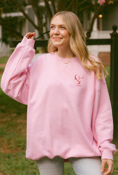 Woman wearing pink sweater with positive messaging that says trust in the process. the design features heart mascot