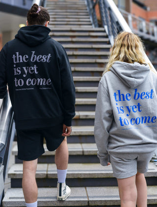 The best is yet to come hoodie in grey and black. Man and woman wearing positive mental health hoodies walking up stairs